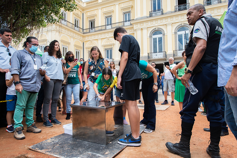 Representativo: Crianças colocando parafusos na Cápsula do Tempo do Museu Nacional/UFRJ com a diretora de Integração Museu e Sociedade, Juliana Sayão